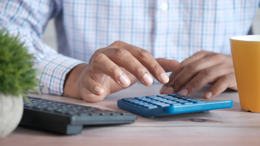 Manos operando una calculadora sobre un escritorio de trabajo